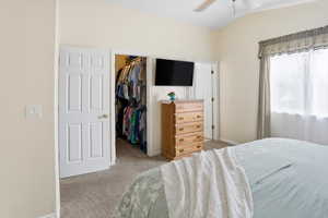 Bedroom featuring light carpet, a walk in closet, a ceiling fan, and vaulted ceiling