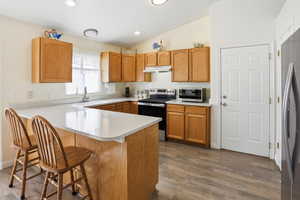 Kitchen with light countertops, a kitchen bar, appliances with stainless steel finishes, a peninsula, and dark wood-style flooring