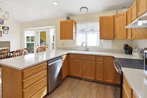 Kitchen featuring light wood finished floors, electric stove, dishwasher, a peninsula, and brown cabinetry
