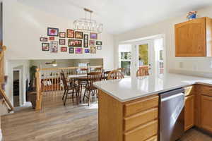 Kitchen with stainless steel dishwasher, light wood finished floors, a peninsula, hanging light fixtures, and brown cabinetry