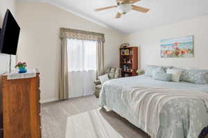 Bedroom with vaulted ceiling, light colored carpet, and a ceiling fan