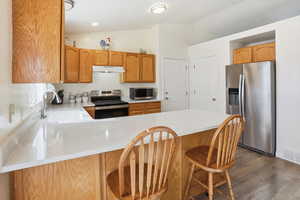 Kitchen featuring stainless steel appliances, lofted ceiling, a breakfast bar area, a peninsula, and dark wood finished floors