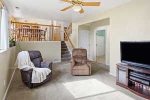 Living area featuring carpet flooring, a ceiling fan, and stairway