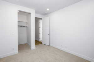 Unfurnished bedroom with a spacious closet, light colored carpet, and recessed lighting