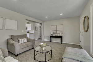 Living area with light colored carpet, recessed lighting, and a textured ceiling