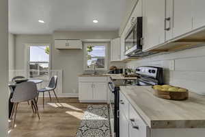 Kitchen featuring black range with electric cooktop, white cabinetry, light wood-type flooring, recessed lighting, and stainless steel microwave