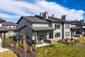 Rear view of house with a chimney, a hot tub, board and batten siding, stone siding, and roof with shingles