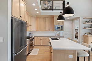 Kitchen featuring light brown cabinets, high quality appliances, recessed lighting, a kitchen breakfast bar, and hanging light fixtures