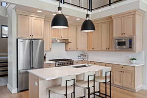 Kitchen with light brown cabinets, appliances with stainless steel finishes, a breakfast bar area, light wood-style flooring, and recessed lighting