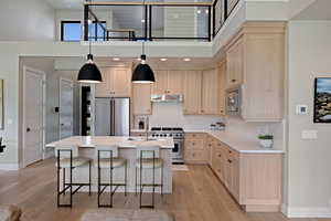 Kitchen featuring light brown cabinets, a towering ceiling, high quality appliances, a kitchen breakfast bar, and decorative light fixtures
