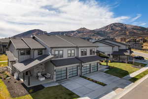 View of front facade with concrete driveway, a front yard, stone siding, and covered porch