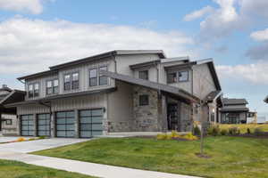View of front facade with a front yard, driveway, stone siding, and a garage