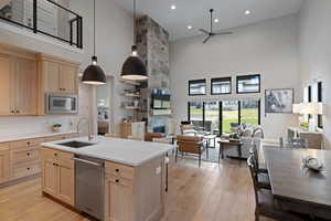 Kitchen with light brown cabinetry, light wood-style flooring, a towering ceiling, open floor plan, and a stone fireplace