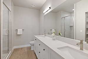 Full bathroom featuring double vanity, wood finish floors, and a shower stall
