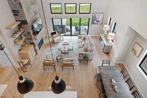 Living room with light wood finished floors, a stone fireplace, and a high ceiling