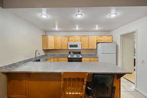 Kitchen with a breakfast bar area, a peninsula, white appliances, light stone counters, and light brown cabinets