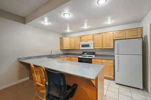 Kitchen with white appliances, light brown cabinets, a peninsula, a kitchen breakfast bar, and light tile patterned floors