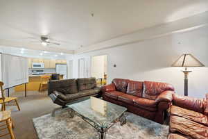 Living area with light colored carpet, a ceiling fan, and a tray ceiling