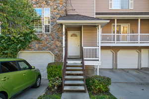 Doorway to property featuring an attached garage, a shingled roof, driveway, and stone siding
