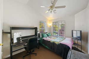 Bedroom with vaulted ceiling, ceiling fan, dark colored carpet, and a desk
