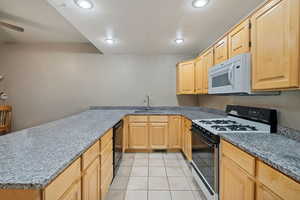 Kitchen with range with gas stovetop, light tile patterned floors, white microwave, a peninsula, and light brown cabinets