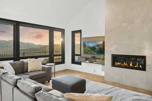 Living room with wood finished floors, a glass covered fireplace, and high vaulted ceiling