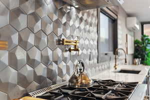 Kitchen view of pot filler, light stone countertops, a wall unit AC, and stovetop with downdraft