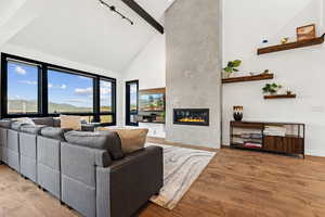 Living room featuring high vaulted ceiling, a fireplace, beam ceiling, and light wood finished floors