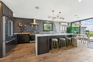 Kitchen with dark brown cabinets, tasteful backsplash, light stone counters, pendant lighting, and appliances with stainless steel finishes