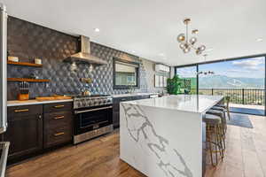 Kitchen with a wall of windows, light stone counters, high end stove, wall chimney range hood, and backsplash