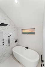 Full bathroom featuring lofted ceiling, a freestanding bath, and a marble finish shower