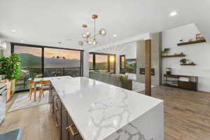 Kitchen with decorative light fixtures, light stone countertops, light wood-style flooring, a chandelier, and a wall of windows