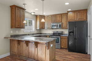 Kitchen with stainless steel appliances, a peninsula, brown cabinetry, pendant lighting, and recessed lighting