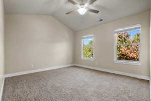 Carpeted empty room featuring lofted ceiling and a ceiling fan