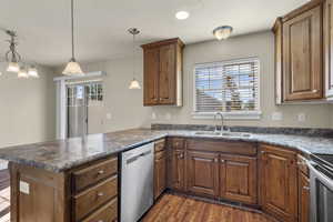 Kitchen featuring dark countertops, a peninsula, appliances with stainless steel finishes, dark wood-type flooring, and brown cabinetry