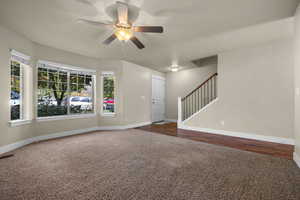 Unfurnished living room with carpet, stairs, and ceiling fan