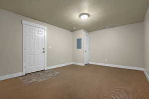 Empty room with a textured ceiling, carpet floors, and electric panel