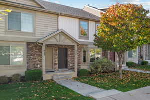 View of front facade with stone siding, a front lawn, and roof with shingles