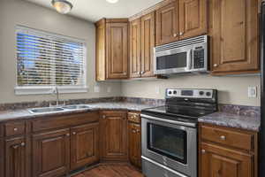 Kitchen featuring stainless steel appliances, dark countertops, brown cabinets, and dark wood finished floors