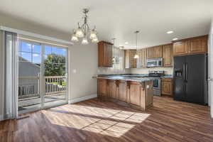 Kitchen with stainless steel appliances, brown cabinets, a peninsula, dark wood-style flooring, and recessed lighting