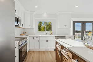 Kitchen with white cabinets, light wood-type flooring, brown cabinetry, recessed lighting, and stainless steel appliances