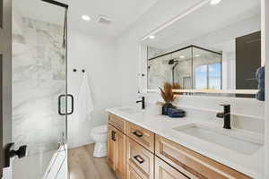 Bathroom featuring a marble finish shower, double vanity, light wood finished floors, and recessed lighting