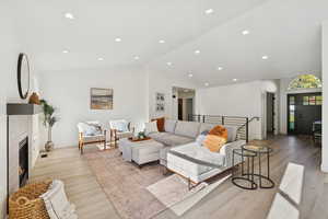 Living room with a glass covered fireplace, light wood-style flooring, high vaulted ceiling, and recessed lighting