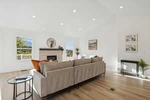 Living room featuring recessed lighting, light wood-style flooring, a tiled fireplace, and high vaulted ceiling