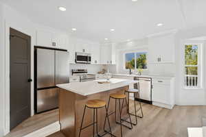 Kitchen with stainless steel appliances, light wood-style floors, a center island, a breakfast bar area, and white cabinetry
