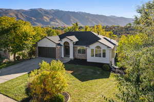 Ranch-style home with a mountain view, driveway, a garage, a front yard, and stucco siding