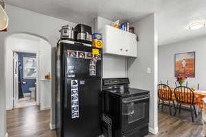 Kitchen with black appliances, light wood-style flooring, arched walkways, white cabinetry, and a textured ceiling