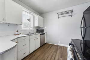 Kitchen featuring black appliances, white cabinets, light countertops, and dark wood finished floors