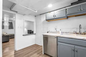 Kitchen featuring stainless steel dishwasher, light countertops, light wood-type flooring, and gray cabinets