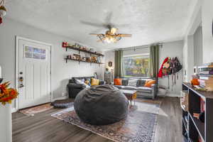 Living area with dark wood-type flooring, a textured ceiling, and a ceiling fan